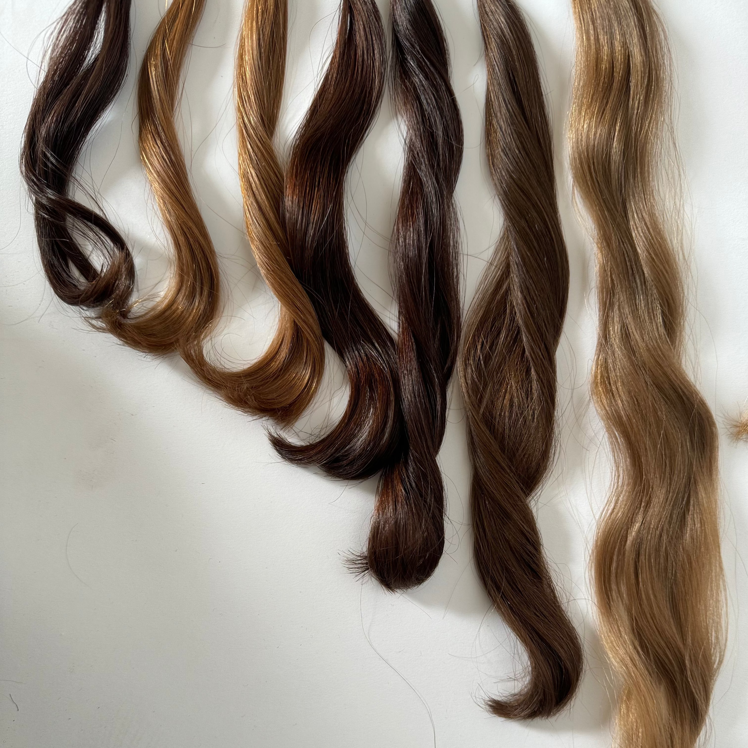 Five synthetic wavy hair extensions in various brown and blonde shades, arranged vertically on a plain white background.